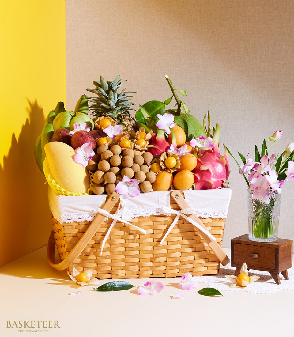 Woven wicker picnic basket overflowing with fresh Thai tropical fruits, mango, pineapple, dragon fruit, and purple orchids