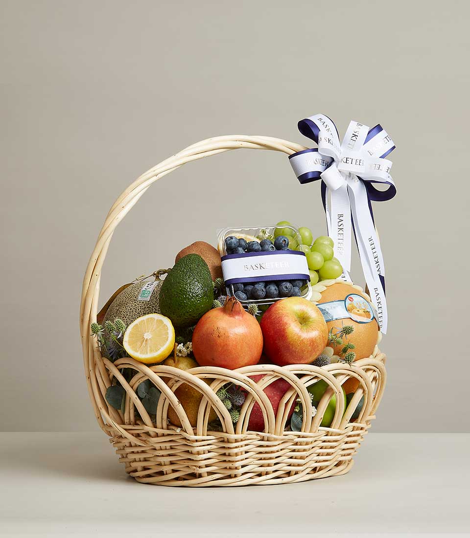 Wicker fruit basket filled with fresh cantaloupe, pomegranates, apples, blueberries, grapes, and tropical fruits with green