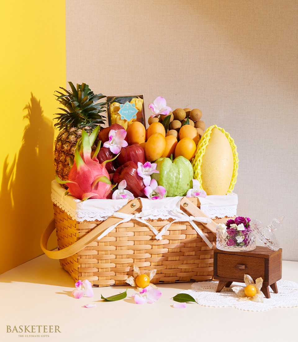 Woven wicker basket filled with tropical fruits, pineapple, dragon fruit, mangoes, and pink orchid flowers