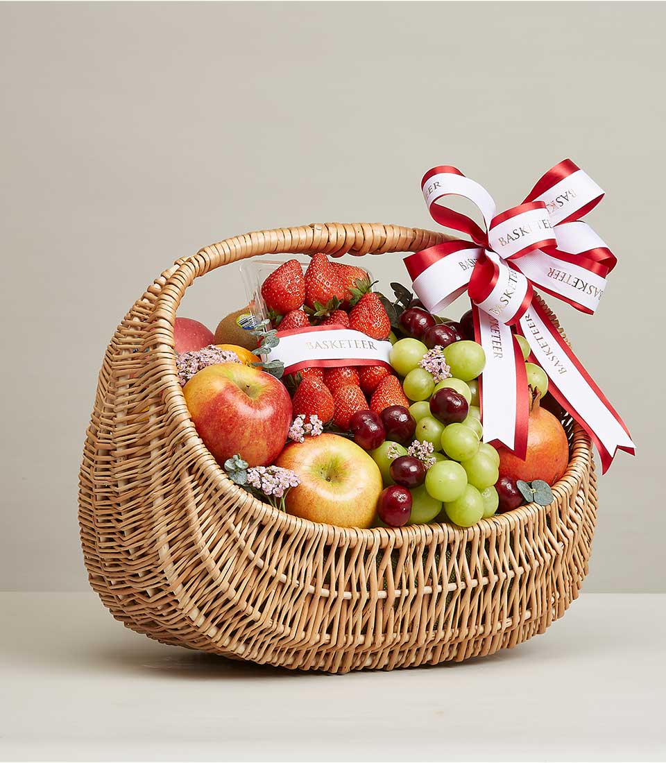 Wicker fruit basket with fresh strawberries, grapes, apples, pomegranate and floral accents tied with Basketeer ribbon