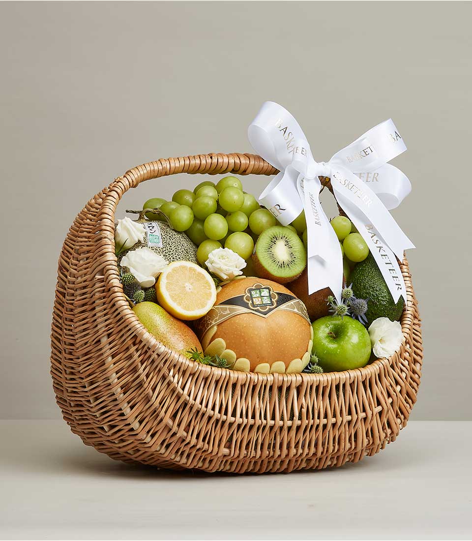 Handpicked fresh fruit hamper with grapes, kiwi, apple, pear and melon in woven wicker basket with white roses