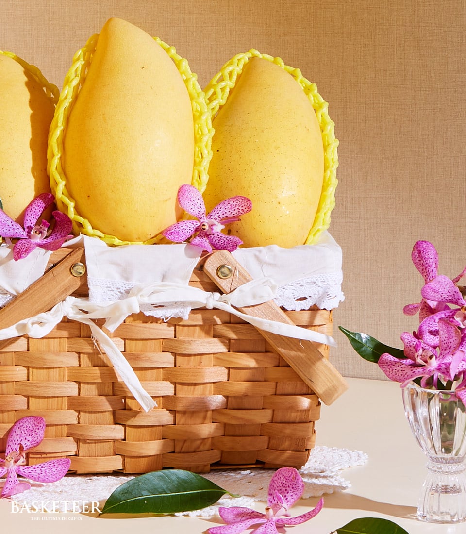 Premium Thai mango gift basket with three ripe yellow mangoes in woven wicker, lined with lace and fresh orchids