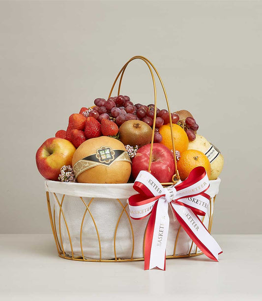 Luxury gold wire fruit basket with fresh strawberries, grapes, apples, kiwis, oranges and pears, tied with red ribbon bow