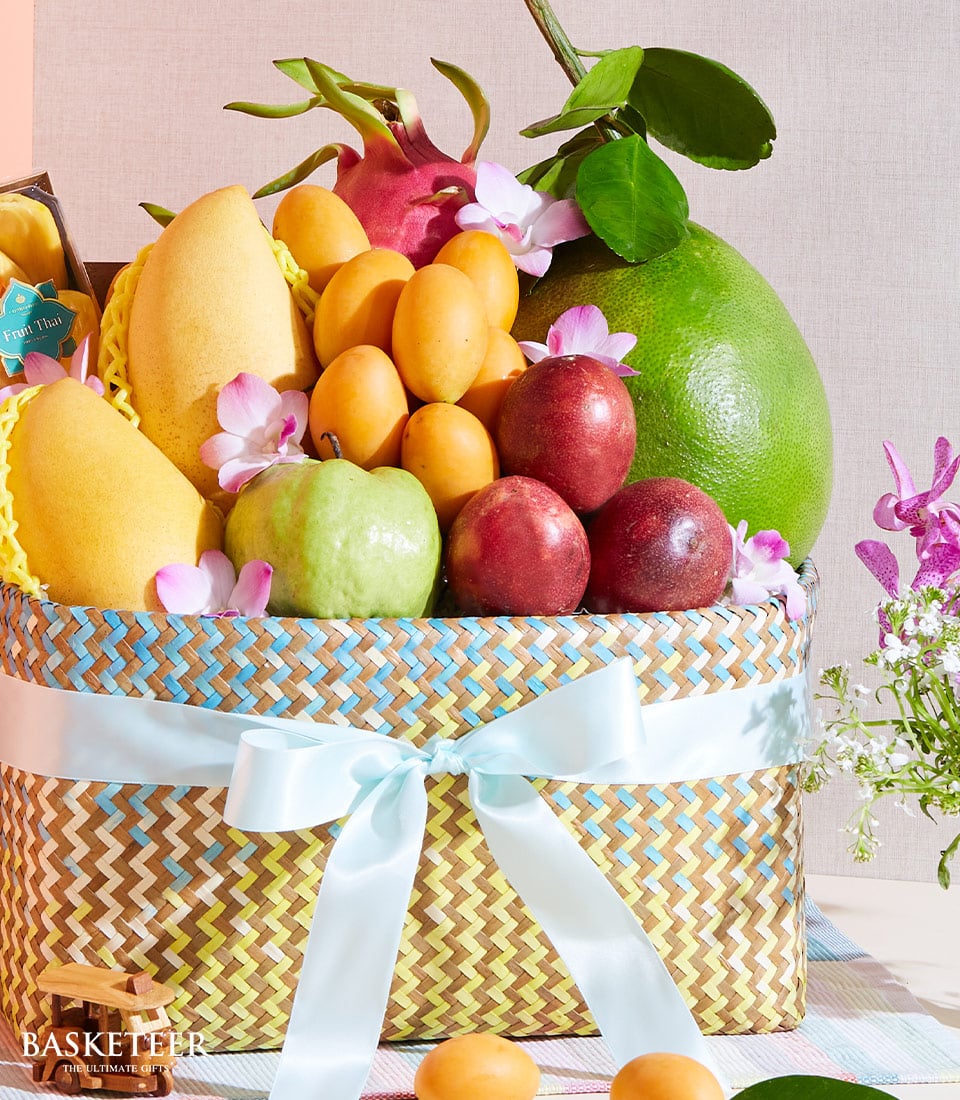 Vibrant woven fruit basket with tropical mangoes, guava, pomelo, and passion fruits, adorned with pink orchids and light