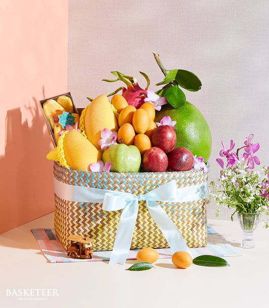 Woven tropical fruit basket with mangoes, dragon fruit, guava, and pomelo, tied with light blue ribbon