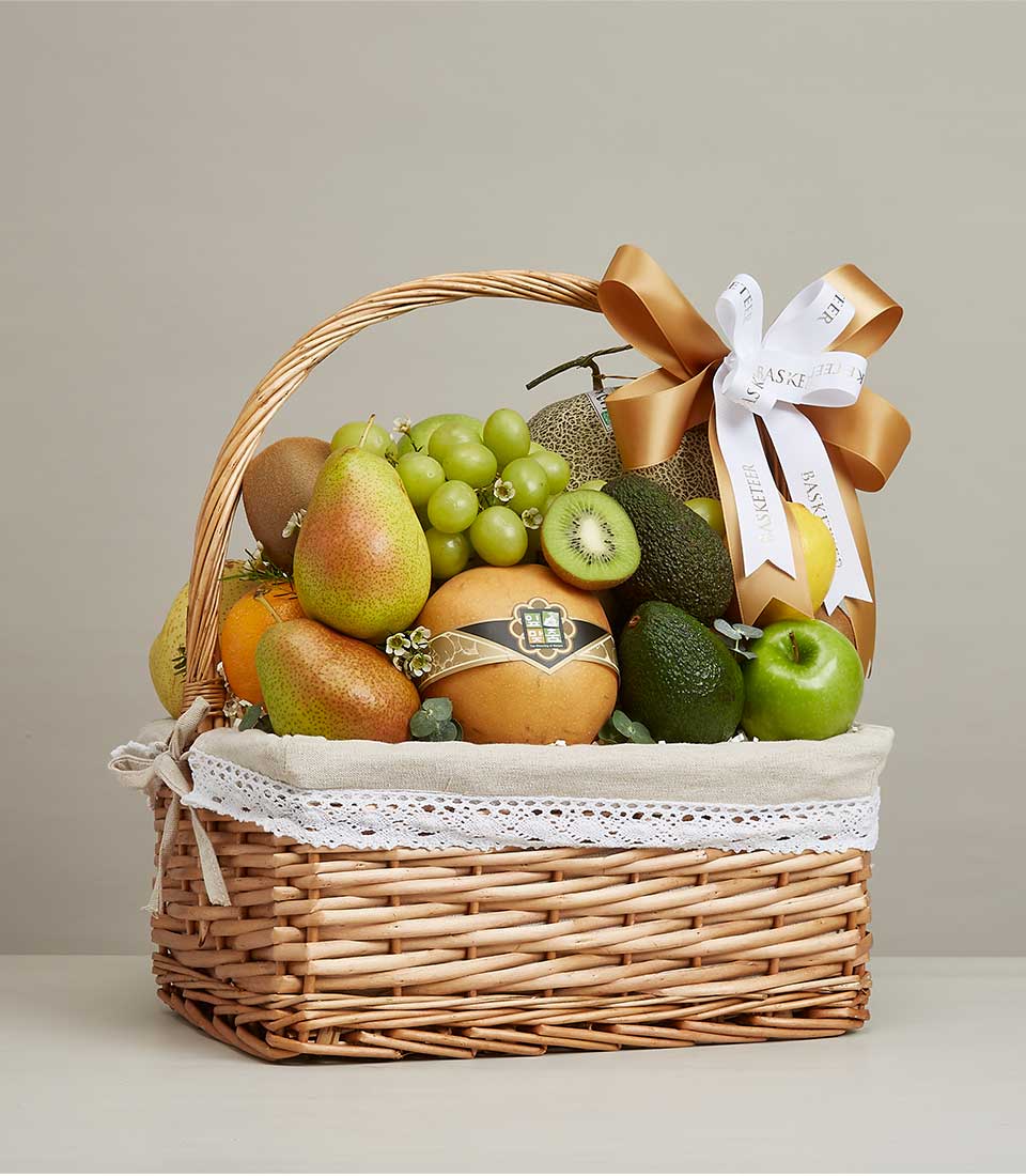 Woven wicker fruit basket with fresh grapes, pears, kiwis, and oranges, tied with gold satin bow
