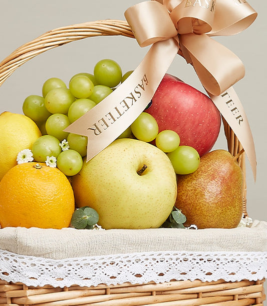 Wicker fruit basket with green grapes, red apple, pear, lemon and tangerine, cream linen lining with gold satin ribbon bow