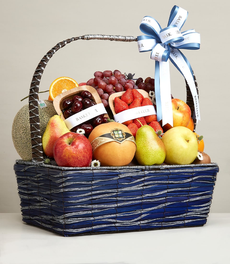 Deep blue woven fruit basket with cantaloupe, grapes, apples, pears, cherries and strawberries, tied with silver ribbon bow