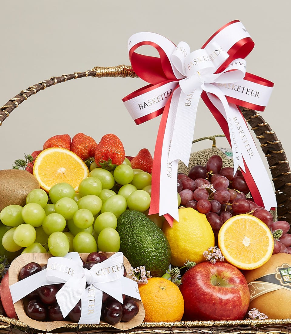 Dark woven premium fruit hamper with red ribbon bow, filled with fresh grapes, strawberries, citrus, and seasonal fruits for