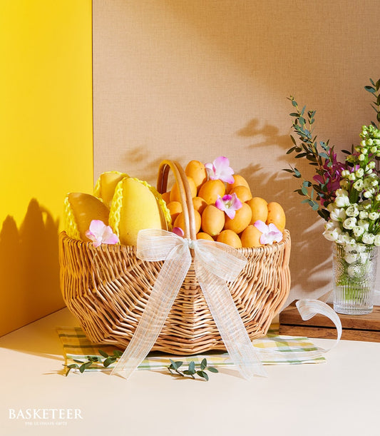 Wicker gift basket with organic Thai mango, marian plum, pears and pink orchids tied with white ribbon