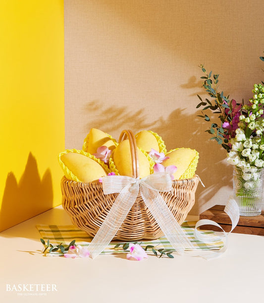 Golden mango gift basket with six ripe tropical fruits, white ribbon, and pink orchids