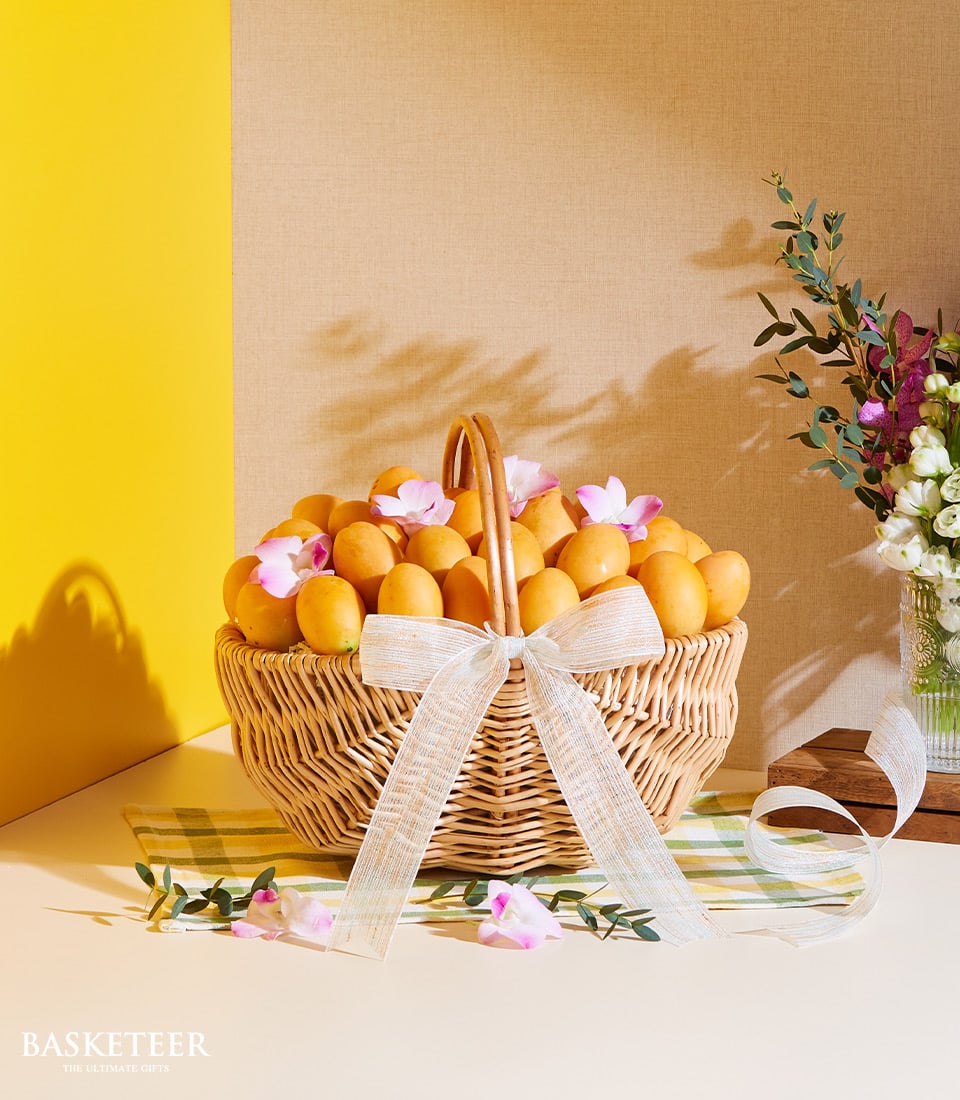 Wicker gift basket overflowing with golden kumquats and fresh pink orchids, tied with sheer striped ribbon