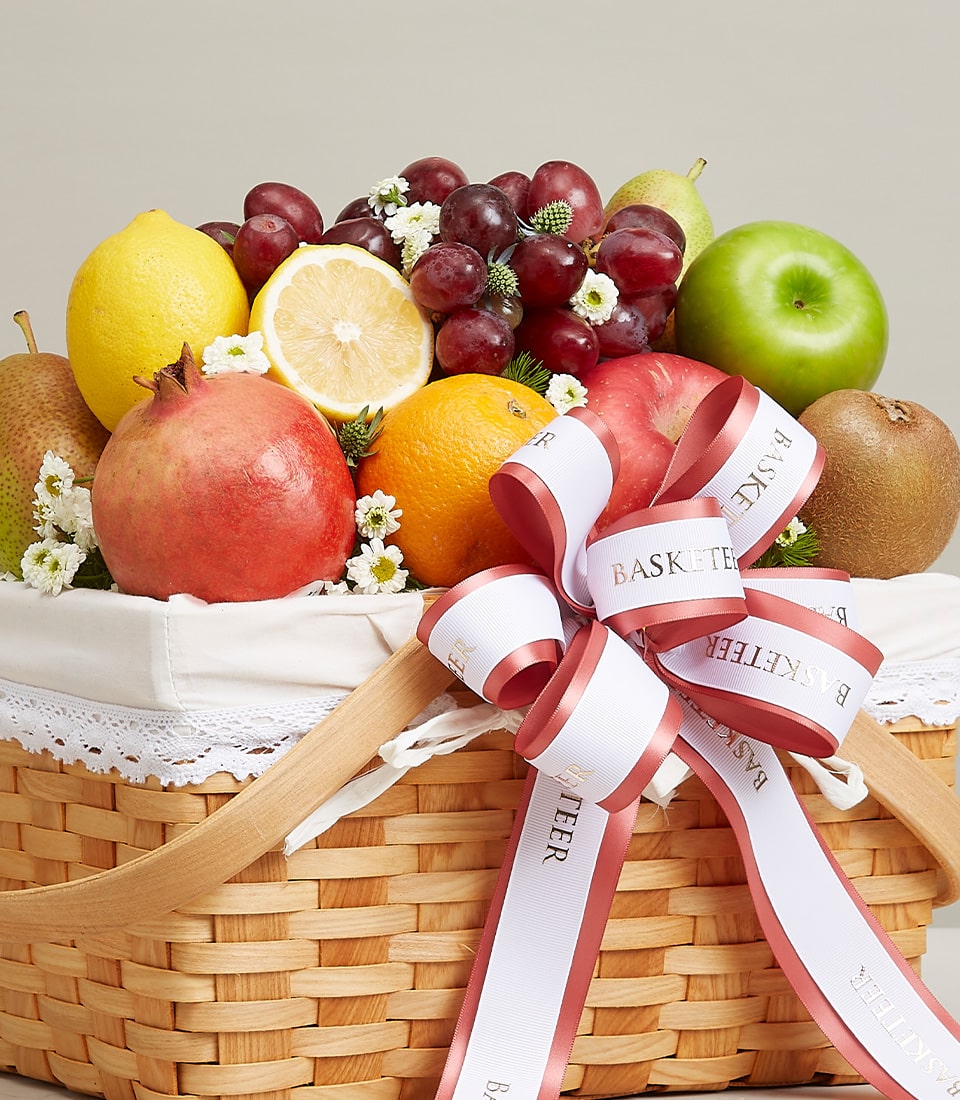 Gala luxury wicker fruit basket with fresh citrus, pomegranate, grapes, and apple, white lace liner, white ribbon bow
