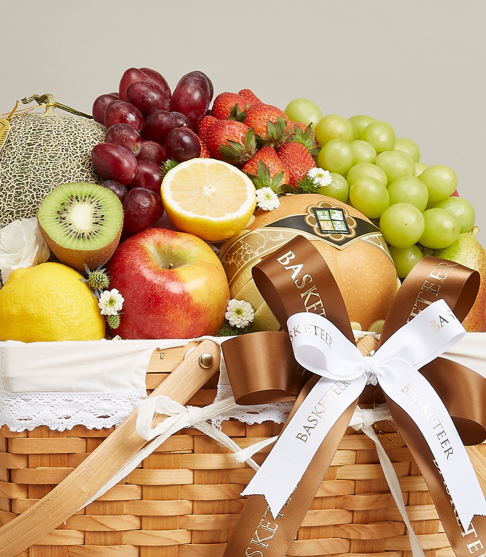Artisanal wicker fruit basket with fresh grapes, strawberries, kiwi, and citrus, adorned with satin ribbon and white flowers