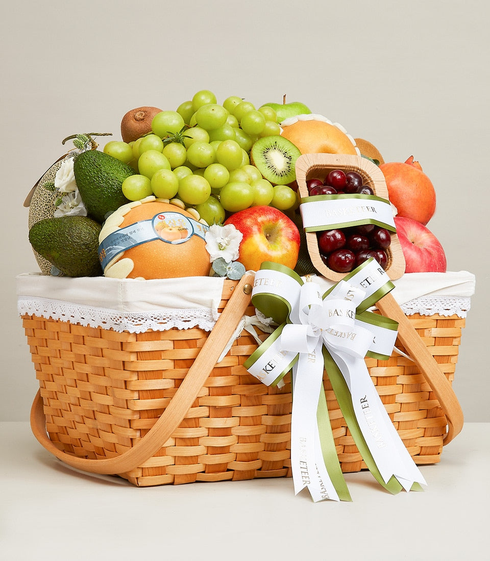 Woven wicker fruit basket with fresh grapes, avocados, apples, pomegranates, kiwi, and cherries, white lace trim, green and