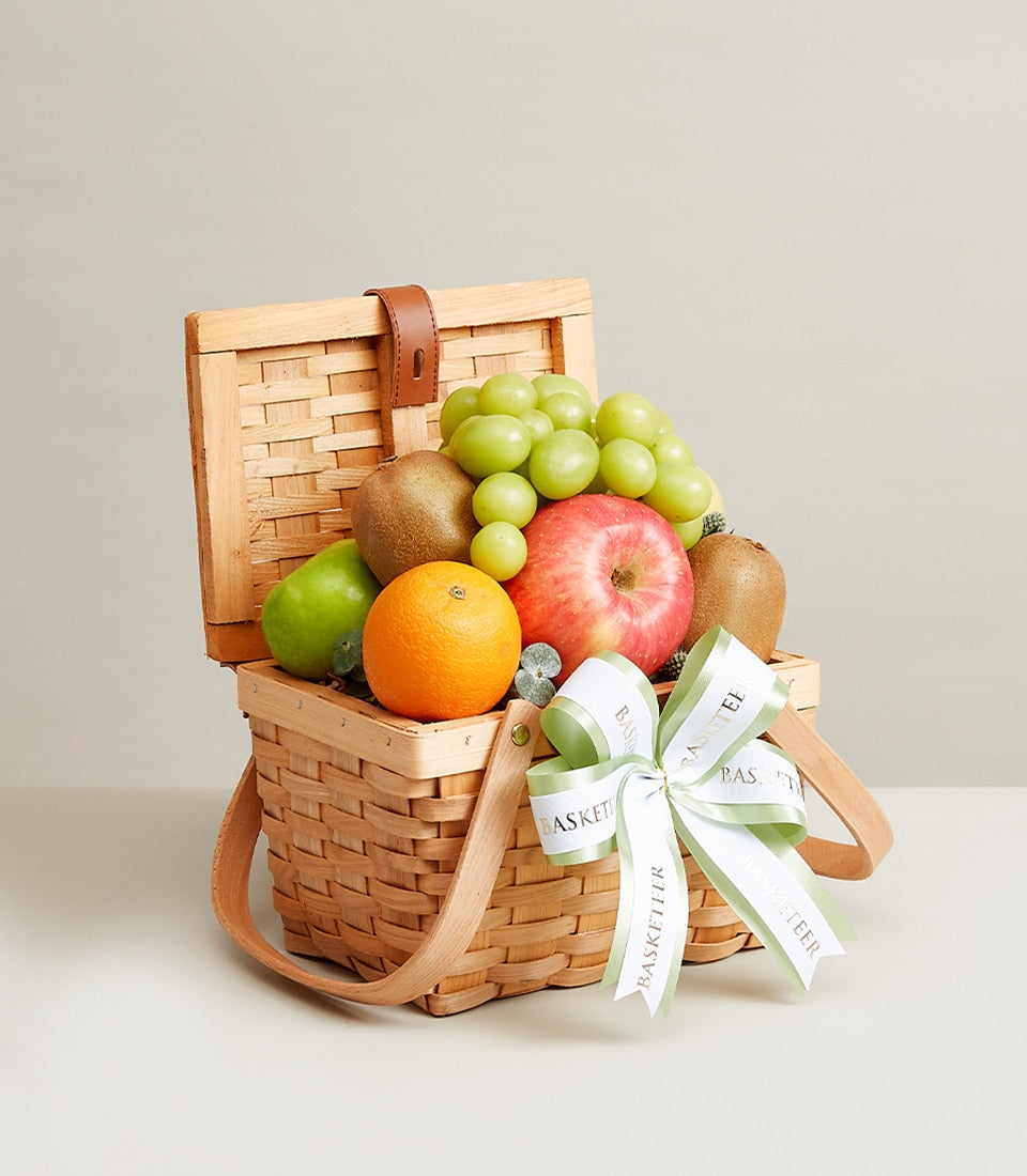 Basketeer fruit gift in a charming wicker basket with an apple, kiwi, grapes, and orange. A perfect premium hamper delivery in Thailand.