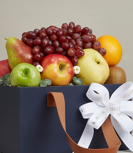 Dark blue luxury fruit basket with fresh grapes, apples, pears, orange and kiwi, accented with white flowers and eucalyptus