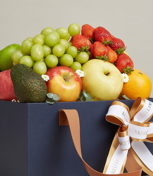 Dark blue luxury gift box filled with fresh grapes, strawberries, apples, pear, avocado and orange, white flowers, gold