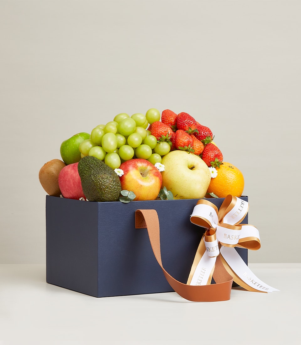 Gourmet fresh fruit medley in dark blue gift box with brown leather handles, green grapes, strawberries, apples, kiwi, pear,