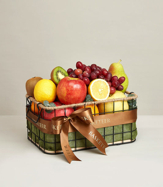 Black wire fruit basket with green fabric lining, fresh red apples, grapes, pears, kiwis and lemons, brown satin ribbon