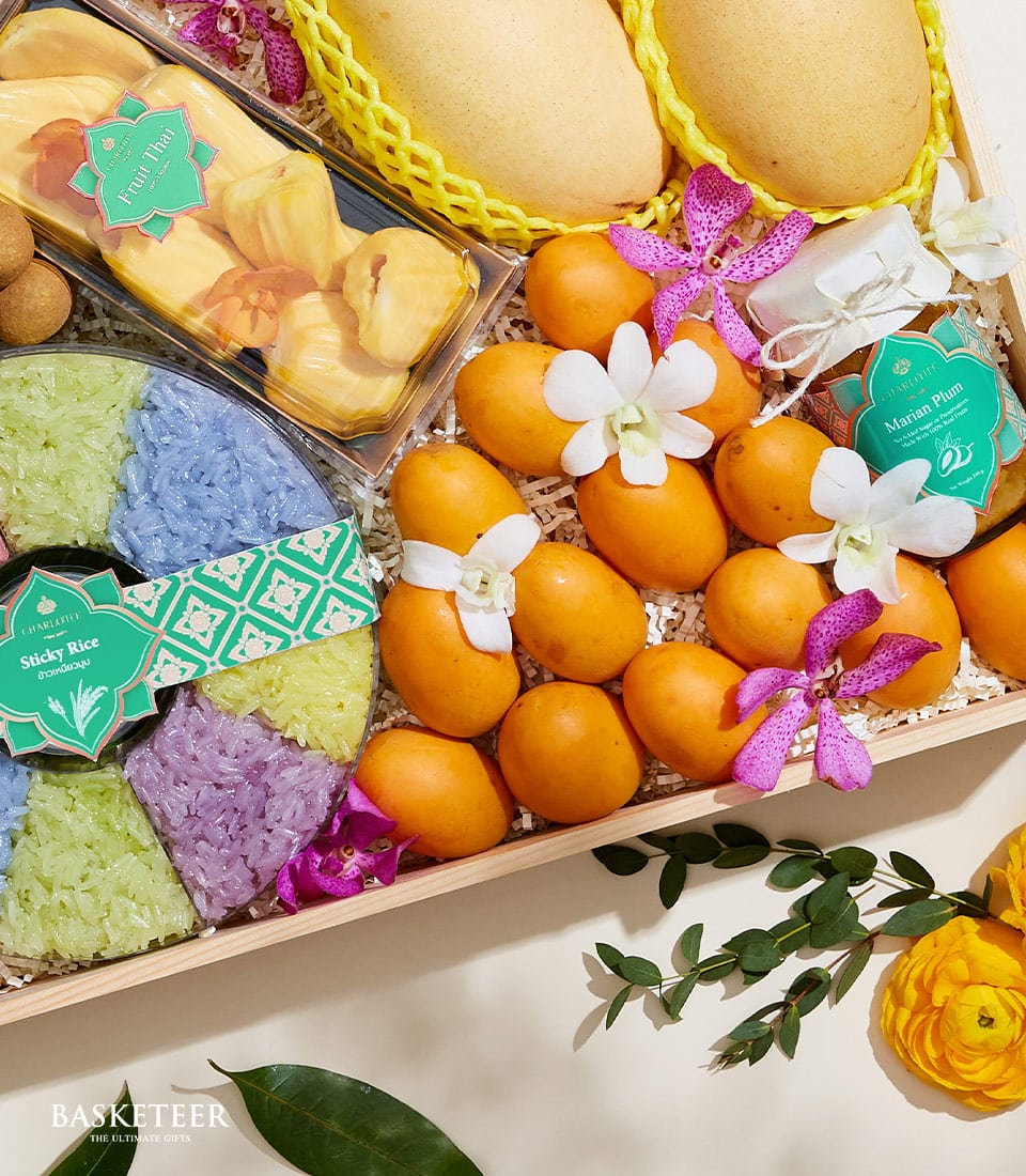 Wooden gift box with Thai mangoes, jackfruit, sticky rice, longan fruits, marian plum preserves, and orchid flowers on white