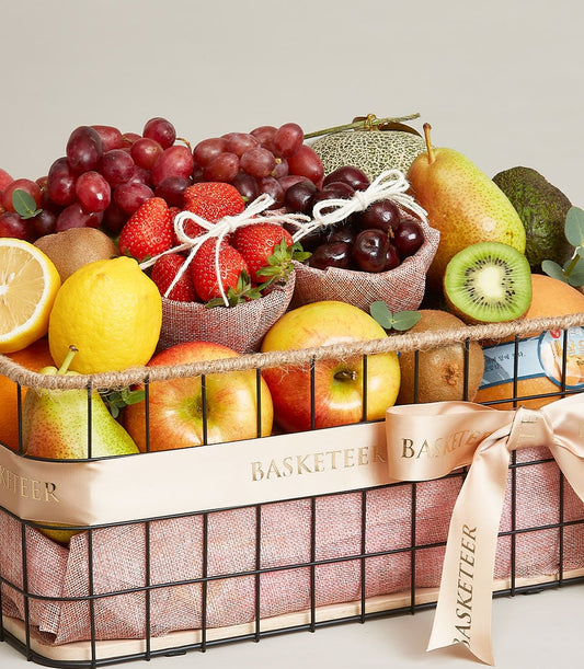 Luxe Fruit Fiesta gift basket with fresh strawberries, grapes, apples, and tropical fruits in black wire frame with peach