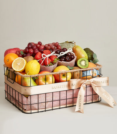 Luxury fruit gift basket with red grapes, strawberries, cherries, apples, citrus, and kiwis in black wire basket with peach