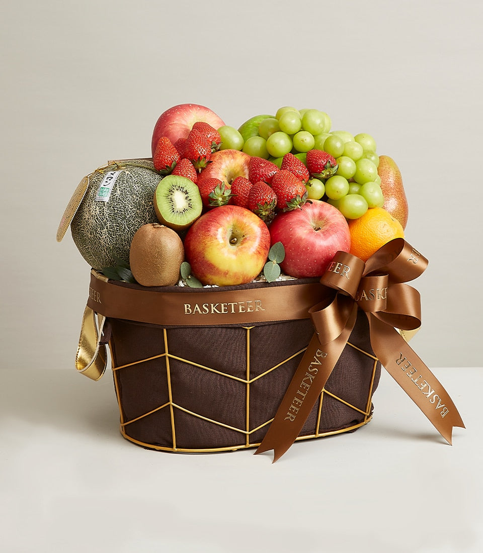 Elegant dark brown woven fruit basket with gold geometric frame, filled with fresh grapes, apples, strawberries, melon,