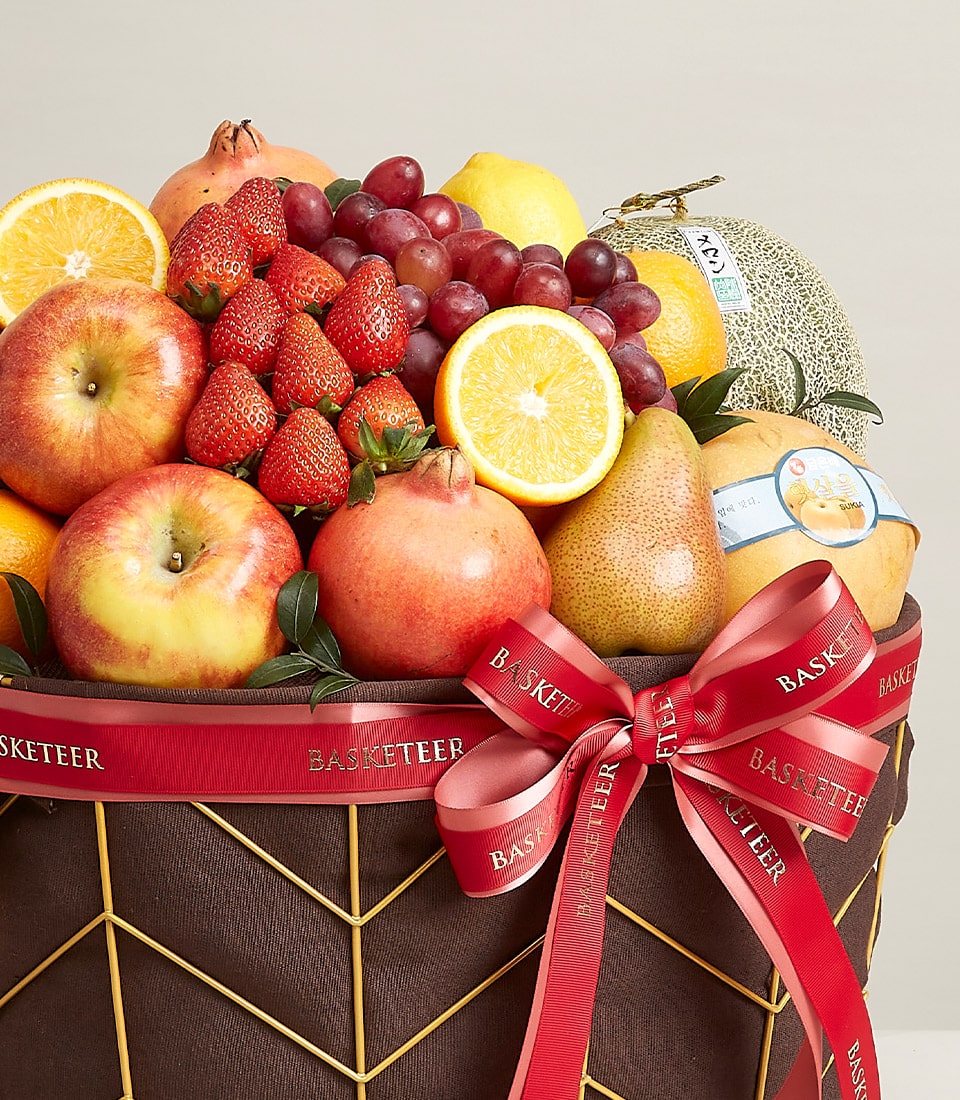 Opulent mixed fruit basket with strawberries, apples, grapes, oranges and pomegranates in gold wire frame with red ribbon bow