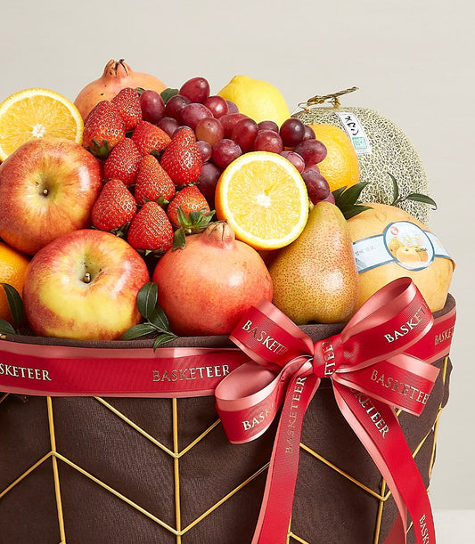 Opulent mixed fruit basket with strawberries, apples, grapes, oranges and pomegranates in gold wire frame with red ribbon bow