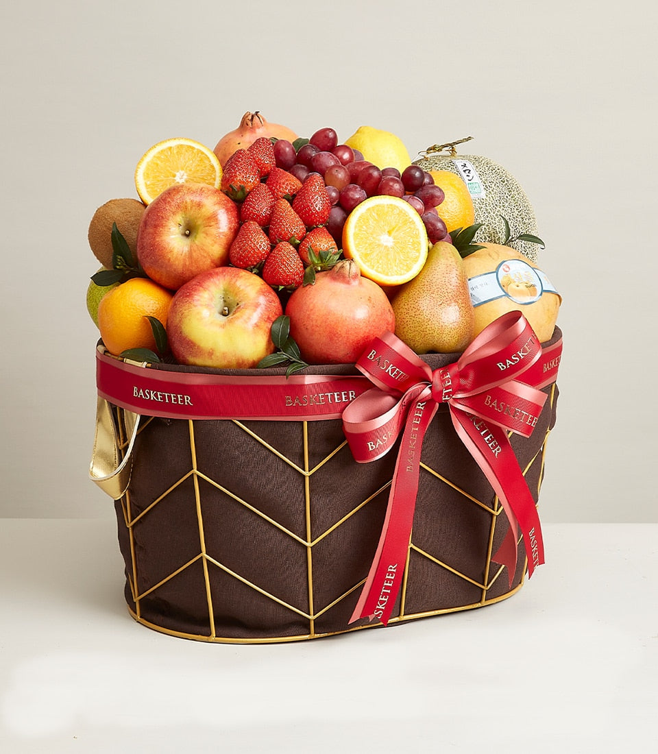 Opulent mixed fruit basket with apples, pomegranates, grapes, and melon in dark brown wicker with gold geometric design and