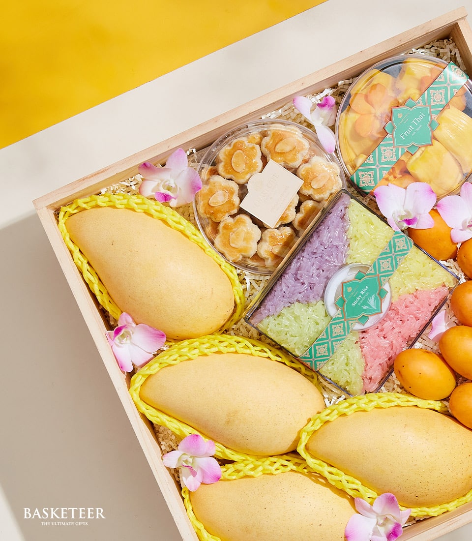 Wooden gift box with ripe Thai mangoes, orchid blossoms, almond cookies, colorful sticky rice, and preserved fruit