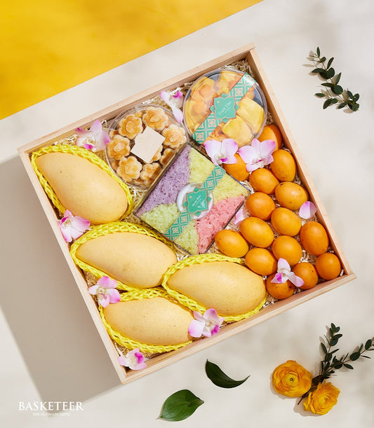 Wooden gift box with Thai mangoes, marian plums, dried fruit, and colorful sticky rice with orchid blossoms