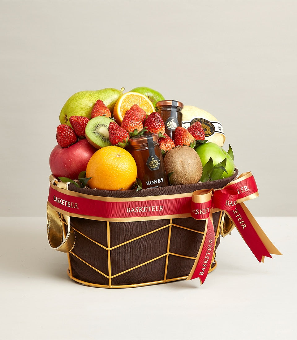 Premium fruit and honey gift basket with apples, pears, oranges, strawberries, and artisan honey in dark gold-trimmed