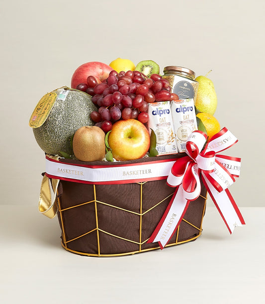 Luxury fruit basket with fresh produce, oat beverage, and honey granola in dark brown fabric basket with gold trim and white