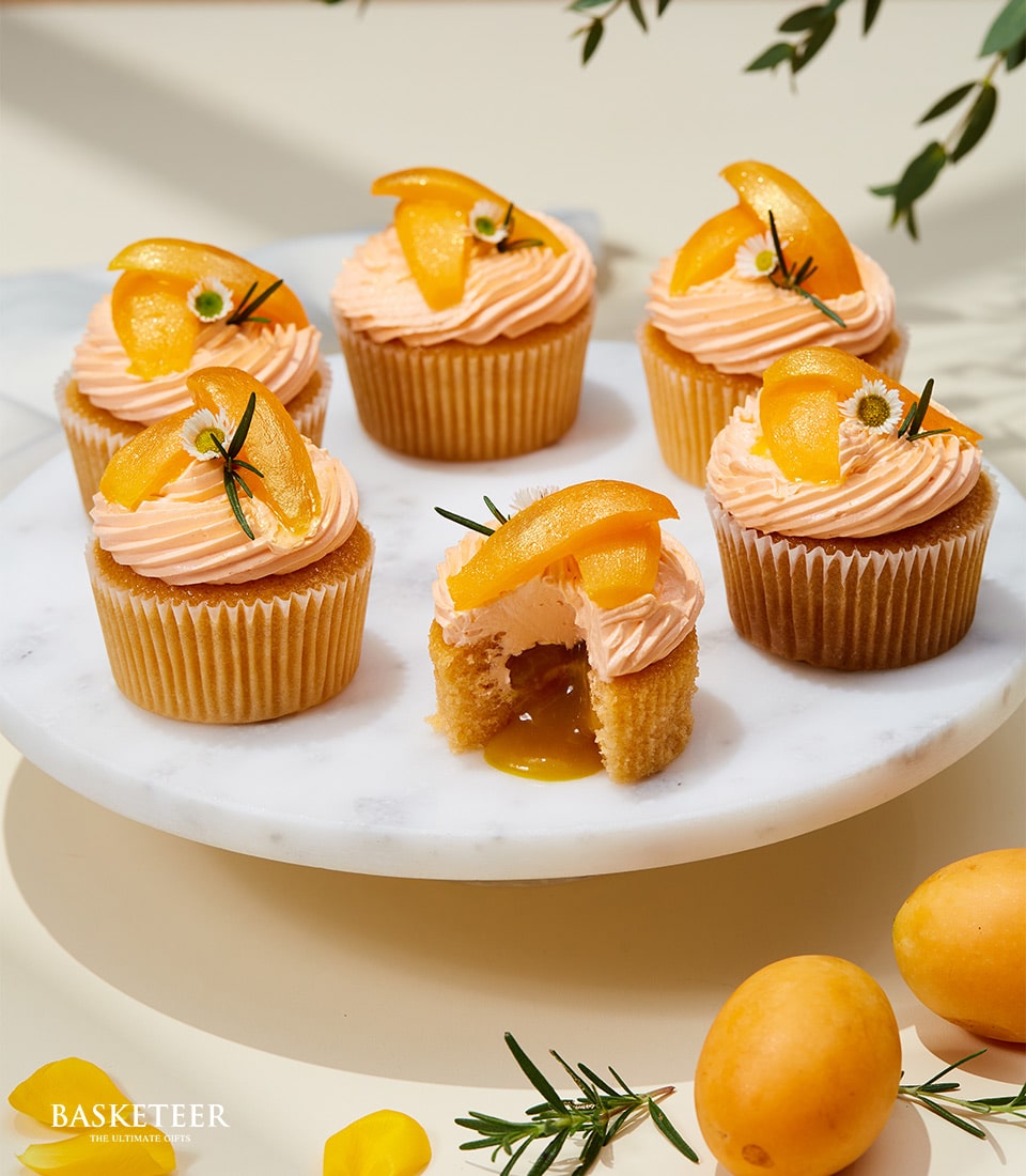 Six apricot cupcakes with fresh fruit and daisy garnish on marble stand, golden filling revealed