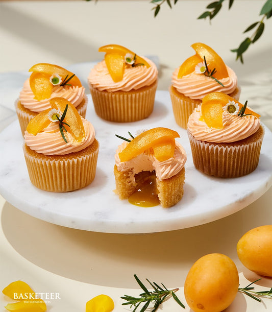 Six apricot cupcakes with fresh fruit and daisy garnish on marble stand, golden filling revealed