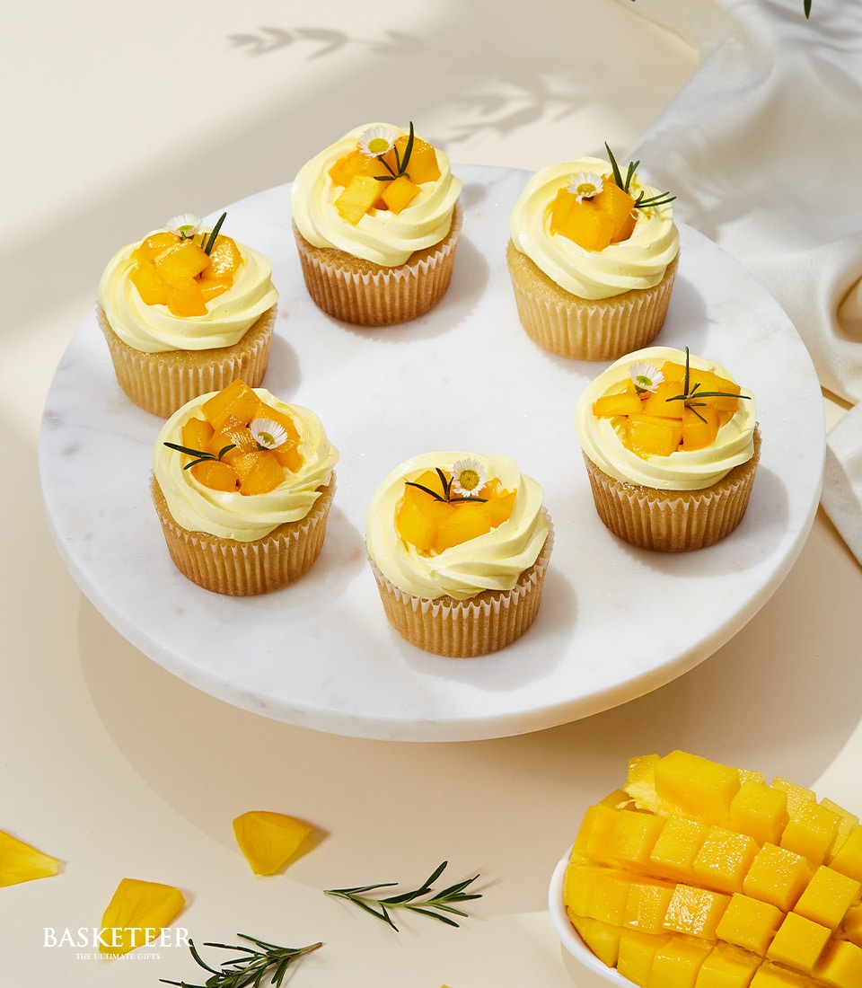 Mango cupcakes with fresh fruit and daisy garnish on marble stand, artisan summer bakery gift