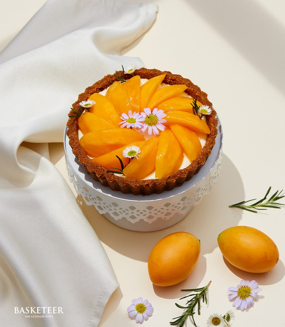 Golden mango tart with creamy filling and spiral fruit topping on ornate cake stand, artisan bakery gift