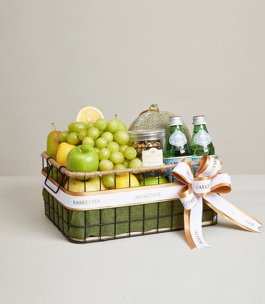 Luxury fruit gift basket with green apples, pears, grapes, nuts jar, and sparkling water with gold-trimmed ribbon