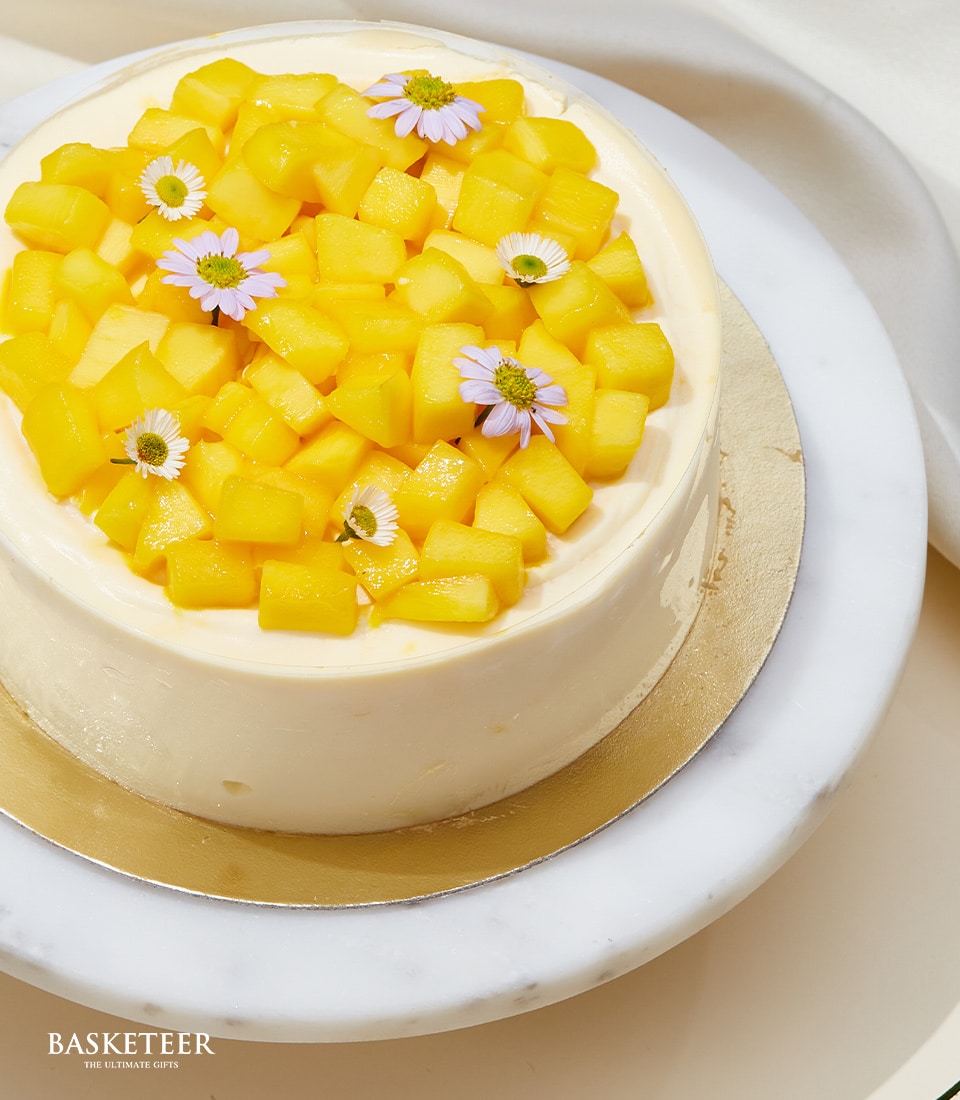 Artisan mango mousse cake from Charlotte Bakery, a British bakery in Thailand. Round pastry topped with fresh mango chunks and delicate purple flowers. Order a custom cake Bangkok!