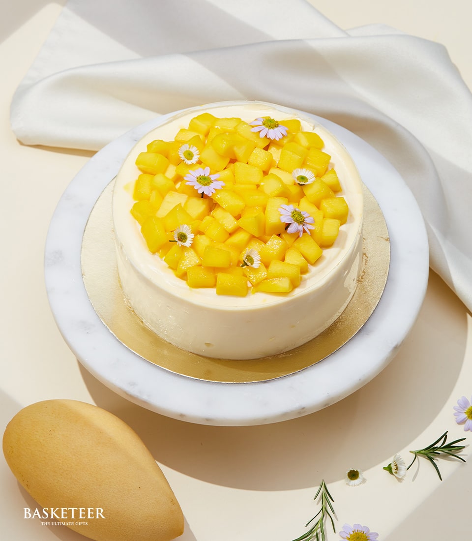 Floral mango mousse cake with fresh diced mango and purple flowers on gold board