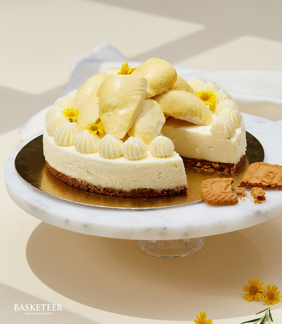 Creamy durian cheesecake with golden crust, white frosting swirls, and fresh durian pieces on marble stand