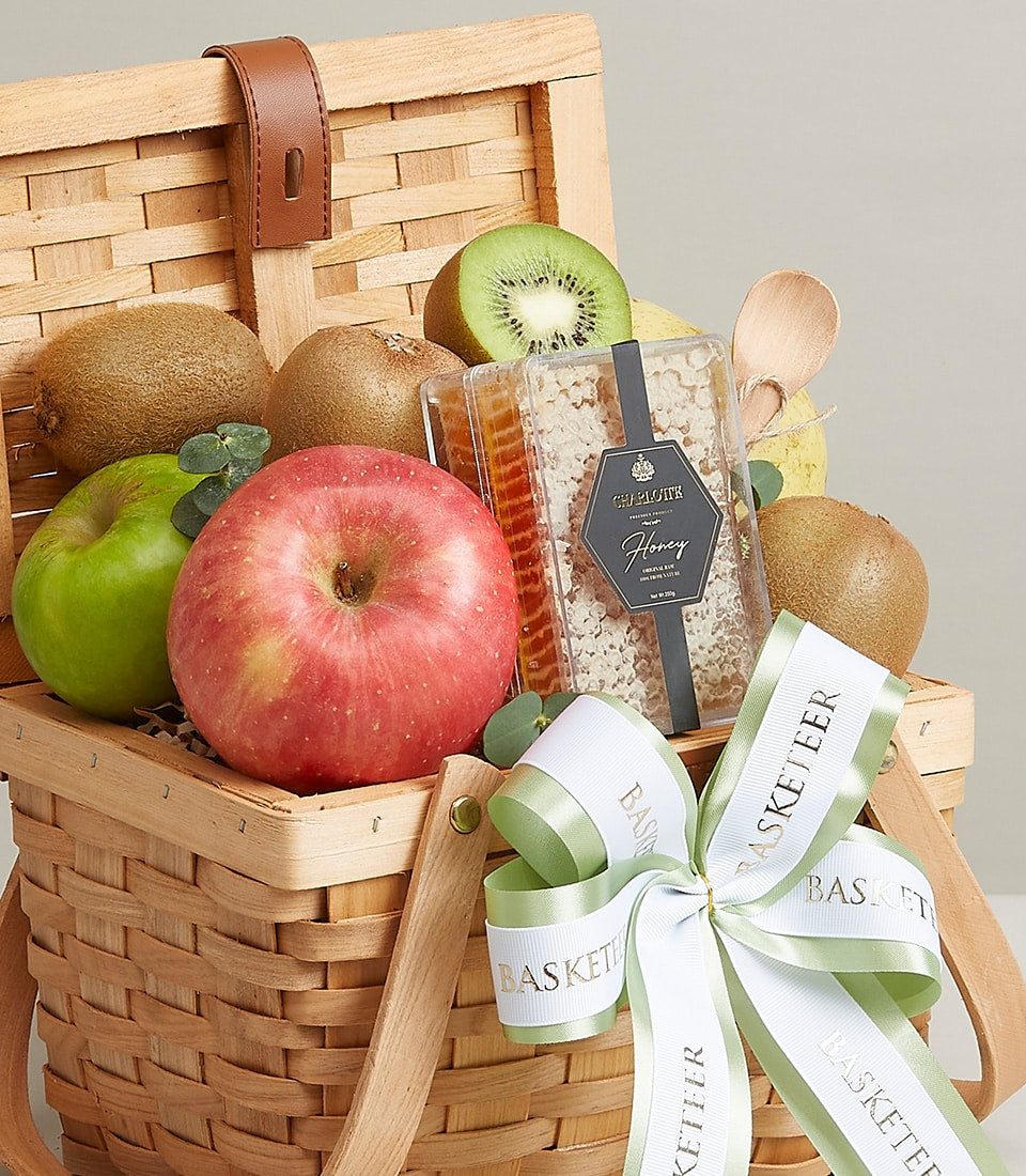 Woven wooden picnic basket filled with fresh kiwis, apples, and premium honeycomb with gold-accented label