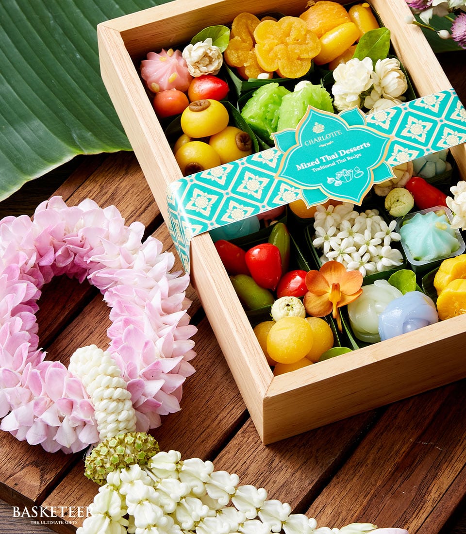 Wooden gift box of colorful Thai desserts in leaf cups with pink and white flower garlands for Songkran celebration