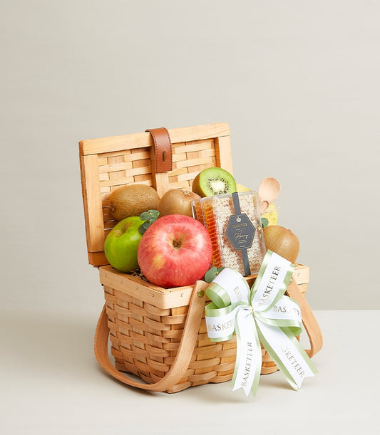Woven picnic basket filled with fresh kiwis, apples, and honeycomb honey gift hamper