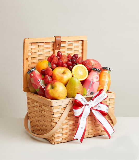 Woven wooden gift basket filled with fresh fruits, juices, and healthy beverages with leather handle and bow