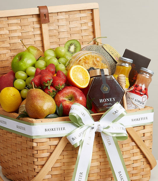 Wicker fruit gift basket with fresh apples, grapes, strawberries, pears, melon, honey jar and gourmet beverages