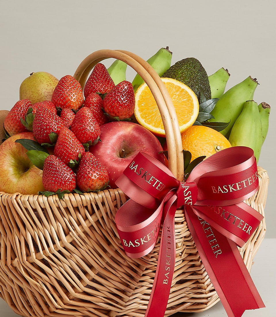 Woven wicker fruit basket with fresh strawberries, apples, pears, oranges, and avocado, tied with red Basketeer ribbon