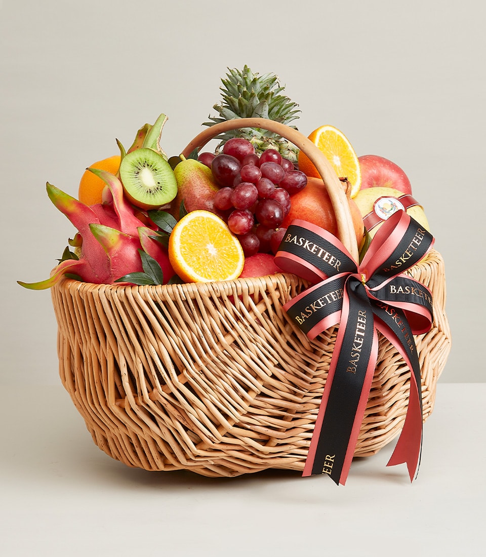Wicker fruit hamper with fresh grapes, oranges, kiwi, pear, dragon fruit, and pineapple